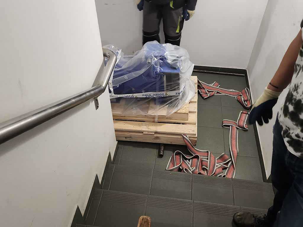 600 kg súlyú liftmotor szállítása lépcsőházban, speciális emelőeszközökkel